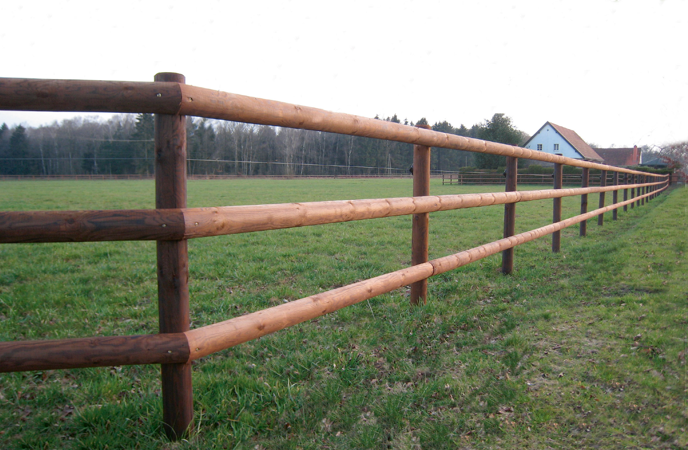 Een lege paddock met op de voorgrond een hek met drie latten.