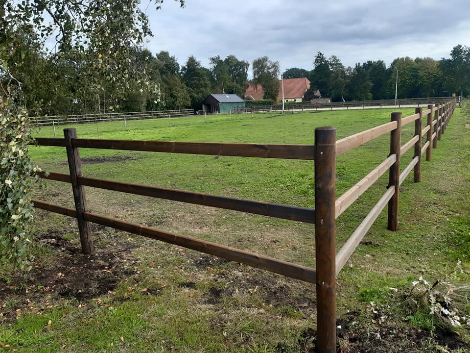 Op de voorgrond is een lege paardenweide met een Colorado paardenomheining. Op de achtergrond staat een villa.