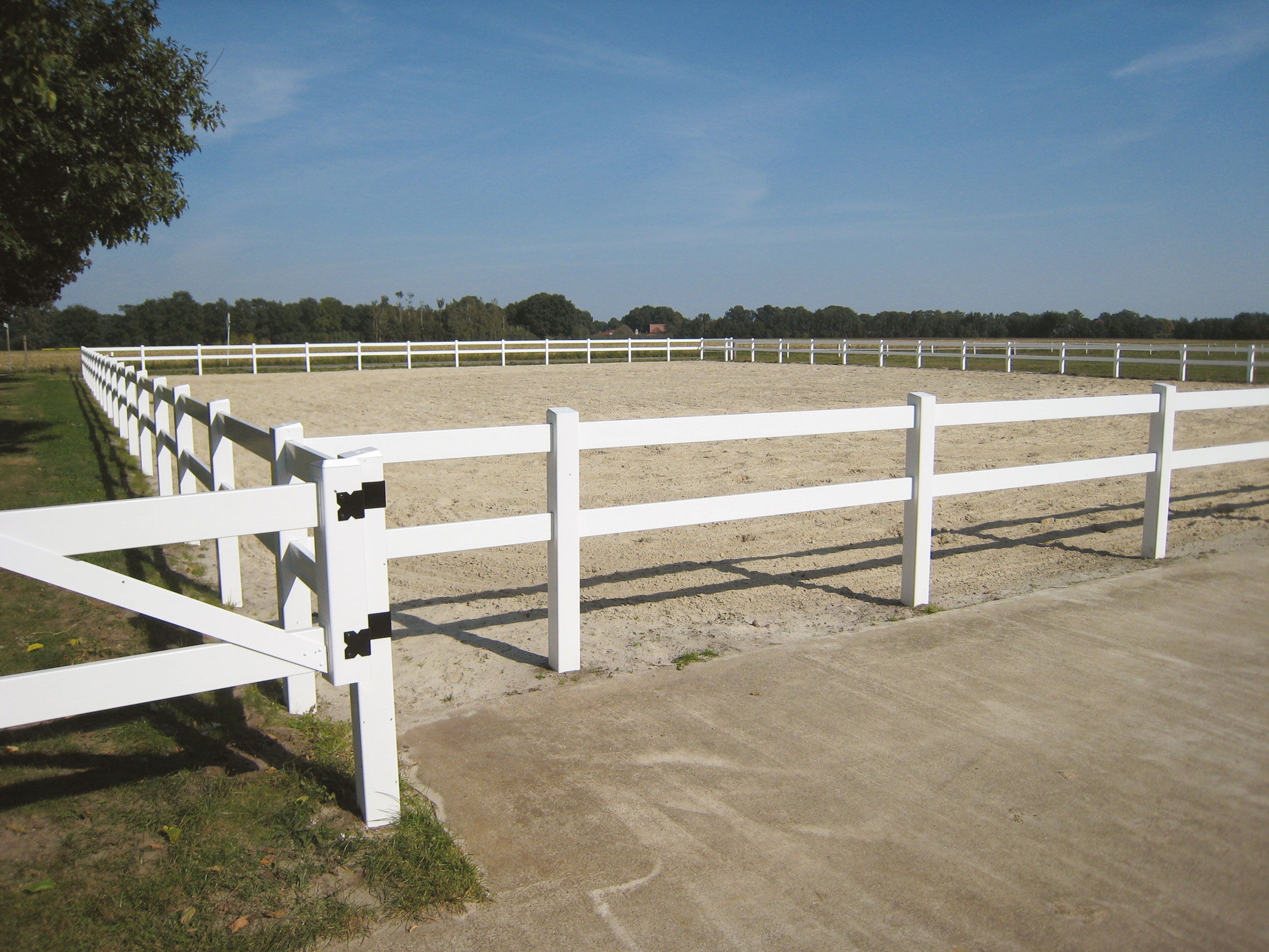 Een wit plastic paardenhek omringt een rijbaan.