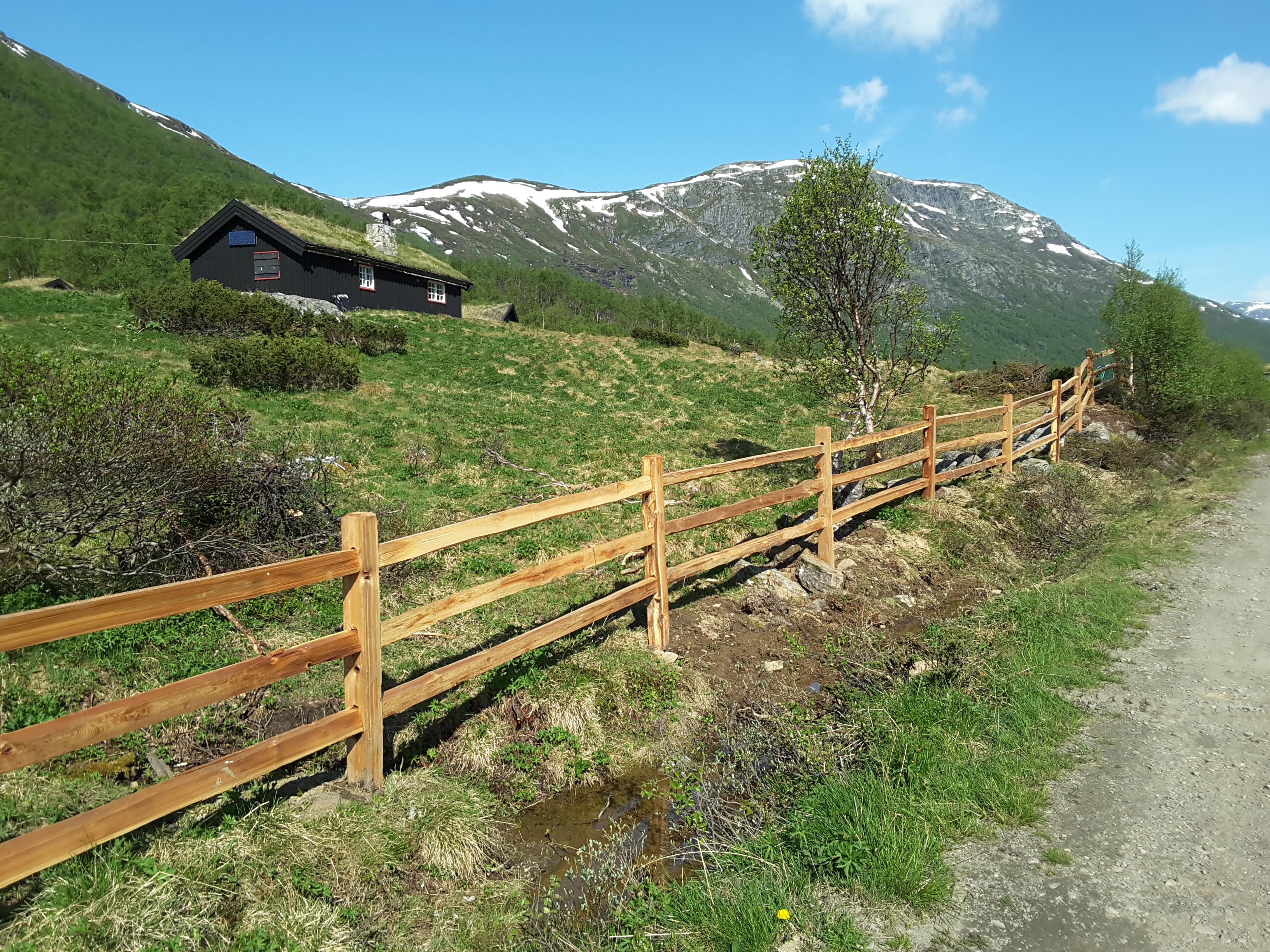 Een rustiek cederhouten hek grenst aan een natuurperceel met een hut in een bergachtig gebied.