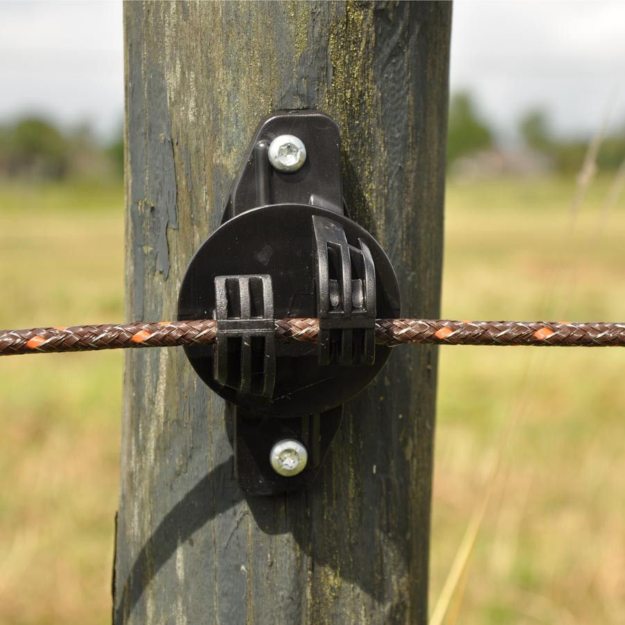 Een elektrische draad voor een elektrische afrastering wordt op zijn plaats gehouden door een isolator op een afrasteringspaal.