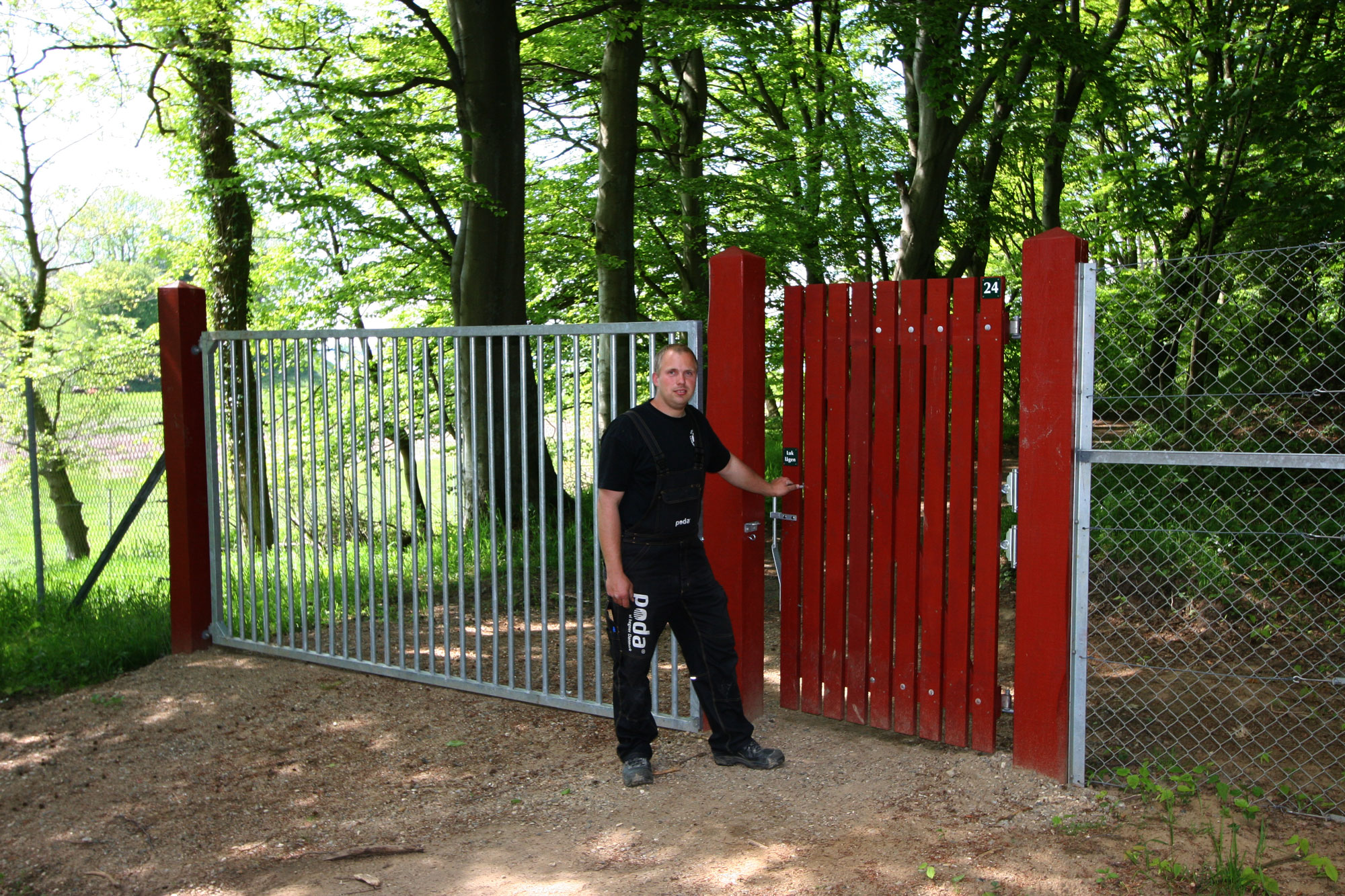 Een man staat voor een rood houten hek dat naar een dierentuin leidt. Naast de poort is een stalen hek.